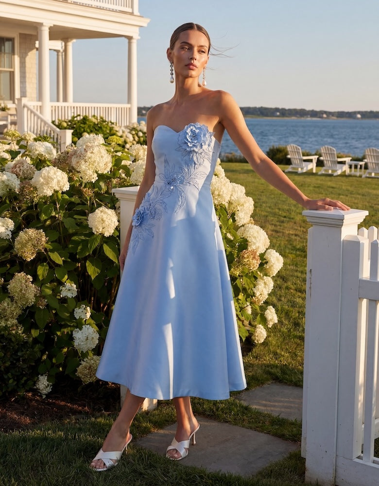 Woman in a light blue strapless dress with floral embellishments standing in a garden.