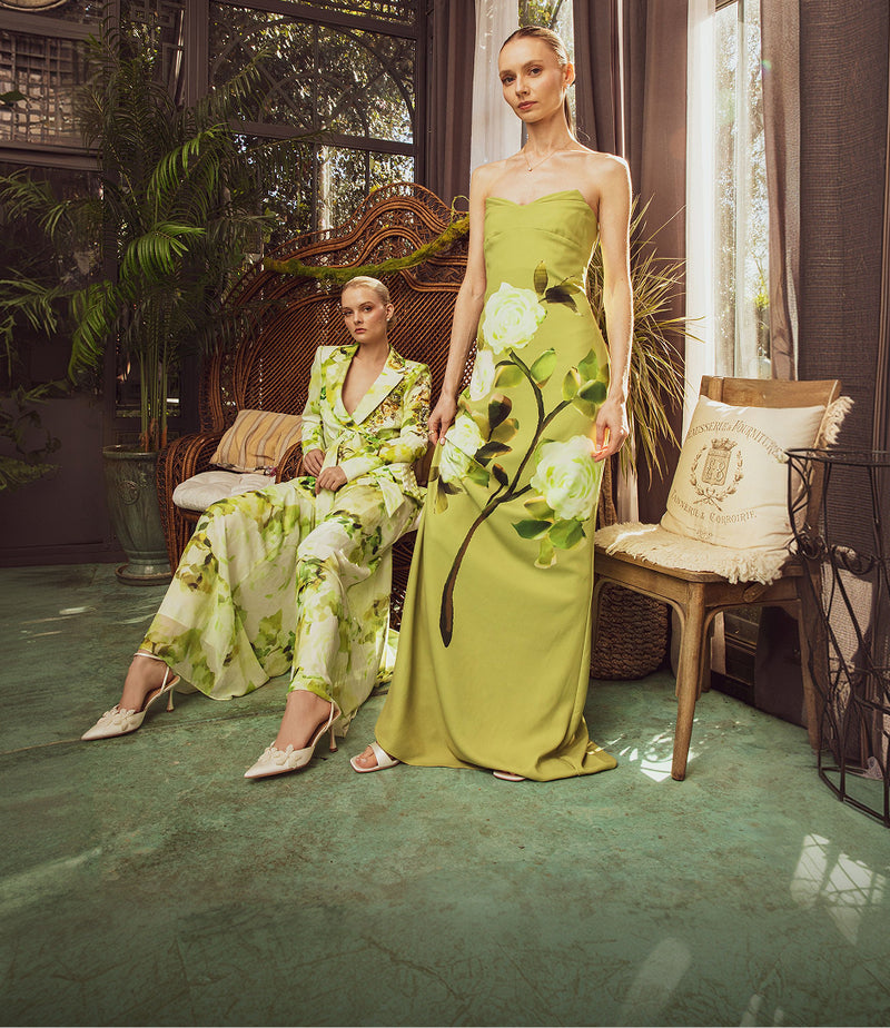 Two women in green floral outfits in a decorative indoor setting.