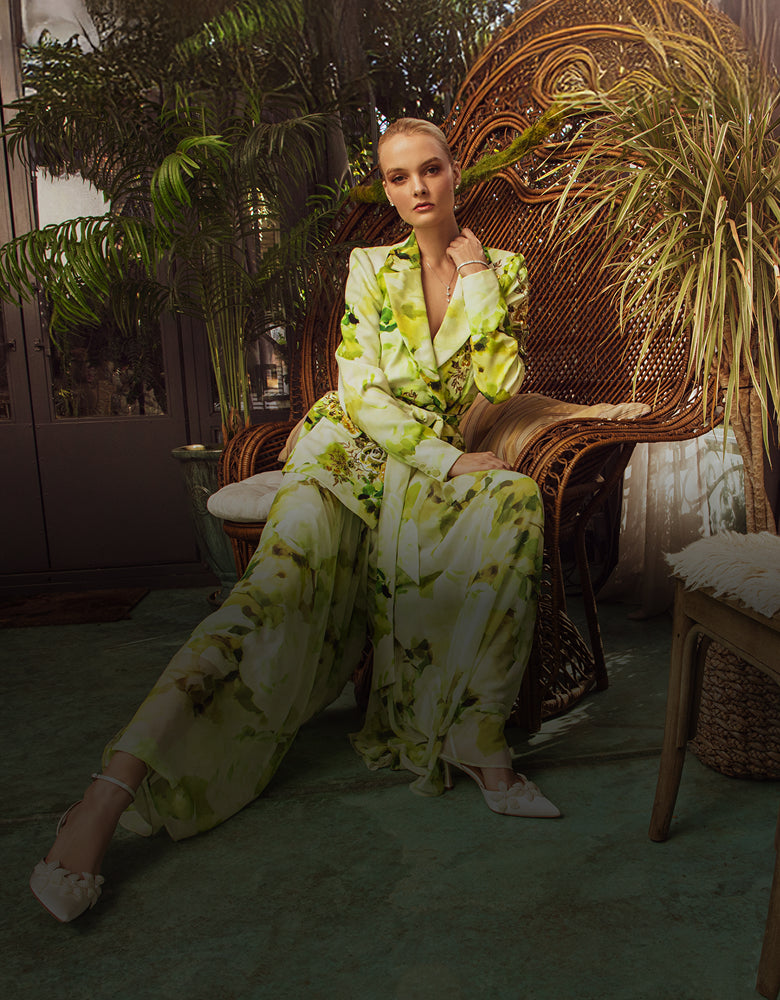 Woman in a floral outfit sitting on a wicker chair surrounded by plants.
